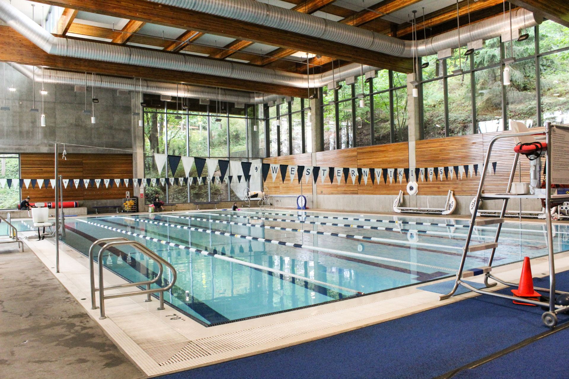 WWU Rec Center indoor swimming pool in a naturally lit room with a bank of windows high up on one wall. A white and blue triangle flag banner hangs above the pool lanes.