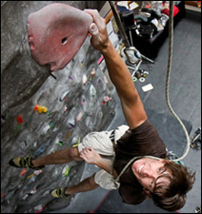 a person holding onto a red climbing hold on the WWU climbing wall