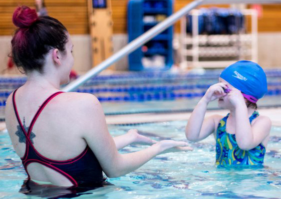A swim instructor in a purple suit and a child in a blue suit and blue swim cap in the WWU Rec Center pool