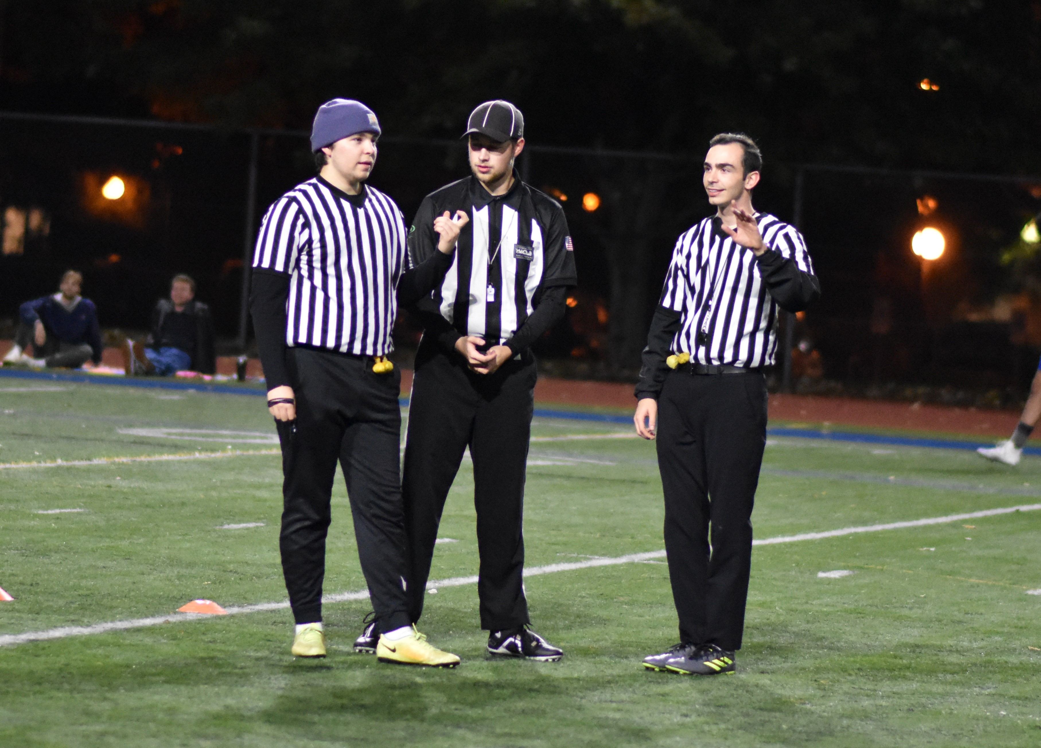 three referees in uniform on the WWU track field discussing a penalty