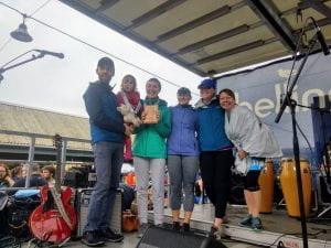 Give til it Hurts Team at the Bellingham Bay Marathon. Group of 5 runners standing on a stage with musical instruments behind them