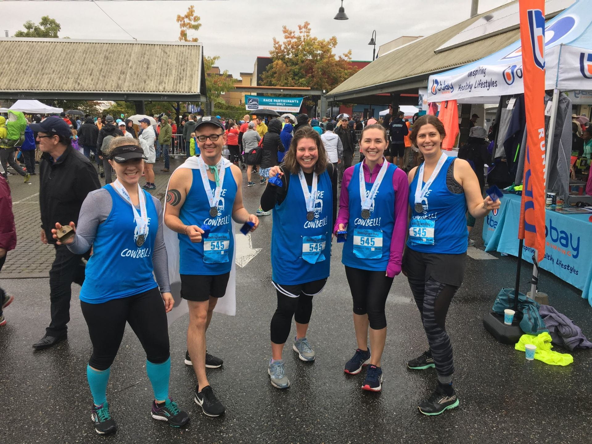More Cowbell Team at the Bellingham Bay Marathon. 5 people in blue shirts with medals hanging around their necks