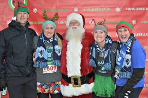 group of 4 runners wearing festive accessories with Santa Claus at the Jingle Bell Run