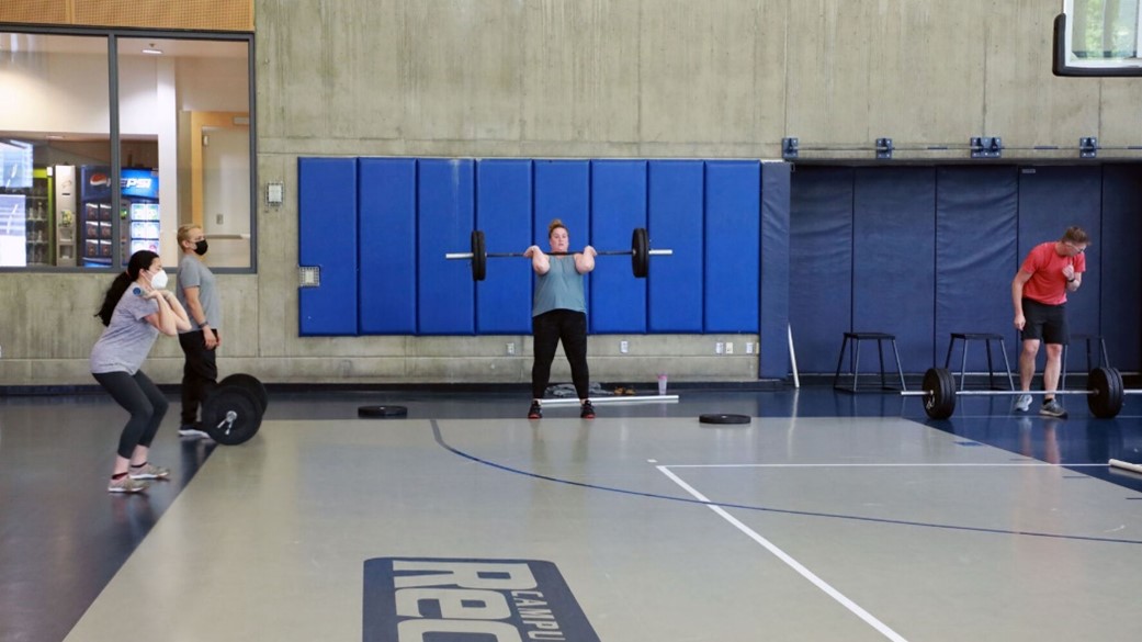 Four patrons lifting barbells in the WWU Rec Center MAC gym.