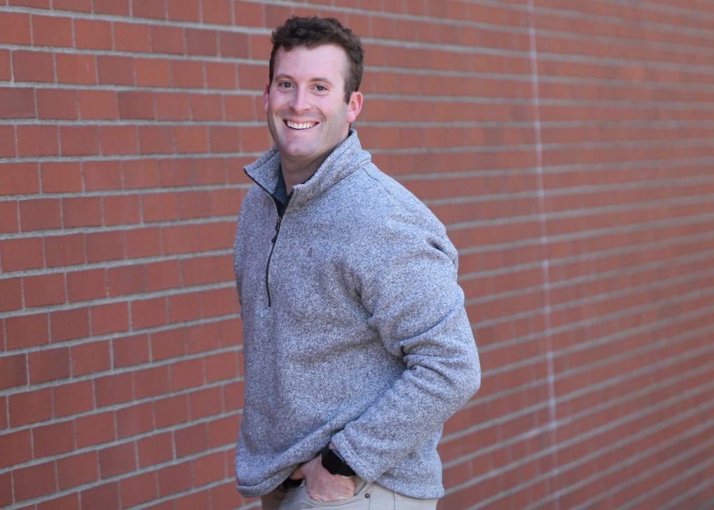 Dane in a grey quarter-zip hoodie standing in front of a brick wall
