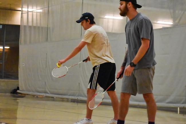 two people holding a birdie and badminton racquet in the middle of a game in the 3-court gym in the WWU Rec Center