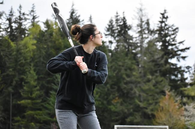 a person with brown hair in a black crewneck holding a black softball bat