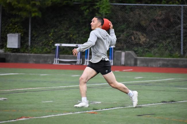 a person in a grey sweatshirt and black shorts on the WWU track field getting ready to throw a kickball