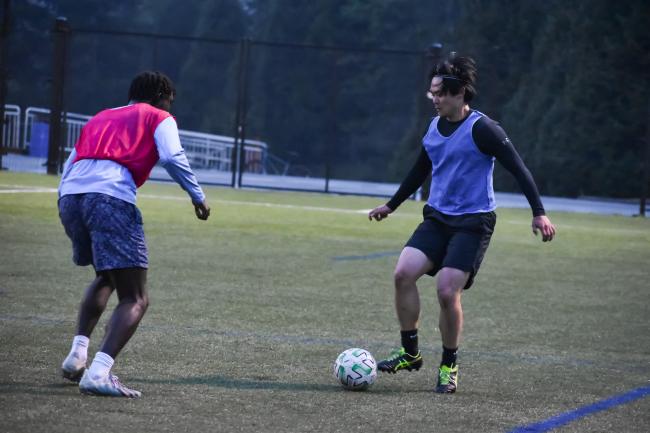 one soccer player in a blue penny dribbling toward another player in a red penny on the WWU track field