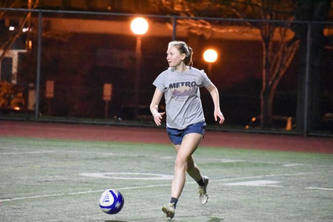 a person with long blonde hair in a grey shirt dribbling a soccer ball on the WWU track field