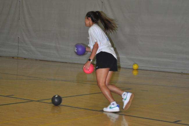 dodgeball player in the 3-Court gym of the WWU Rec Center preparing to throw two balls at opponent with one ball on the ground in front of them