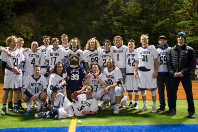 men's lacrosse team posing for group photo on field with bear mascot