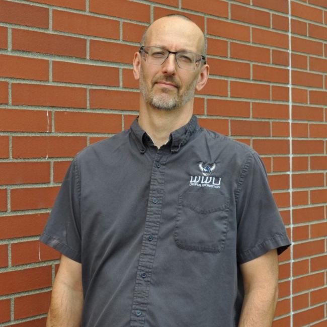 Mike in a grey shirt standing in front of a brick wall