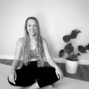 black and white image of Margo posing on a yoga mat with a plant in the background