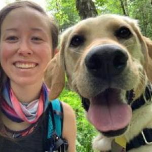Rachel and a yellow Labrador retriever on a hike with greenery in the background